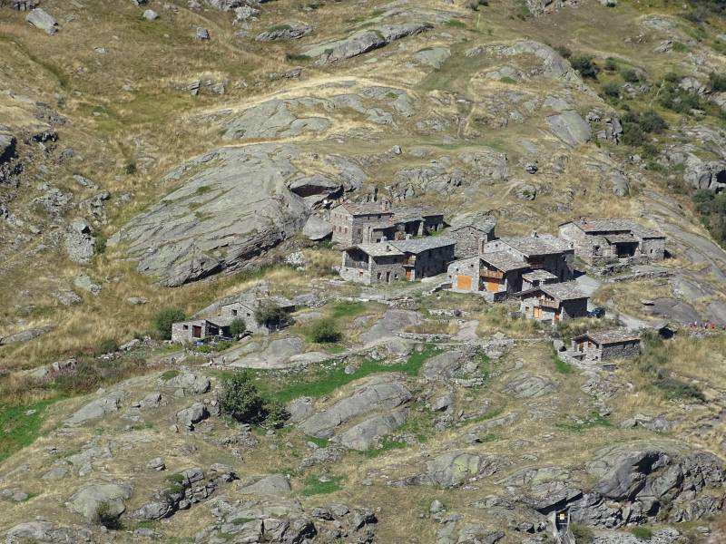 Village rura montagneux complex habitation pente maisons construites flanc montagne sol rocheux pierre toit torchis altitude terres agricoles Scène de paysage présentant une collection d'édifices petits, probablement un village ou un hameau, situés sur un terrain élevé. Ces structures semblent être faites de pierre et sont dispersées dans la zone. À droite se trouve une pente abrupte qui conduit vers le bas vers ce qui semble être une forêt arboricole. L'environnement suggère un cadre rural avec des caractéristiques naturelles telles que des falaises rocheuses et des végétations. Il y a une sensibilité due à l'entourage du paysage. Le ciel est couvert, et il n'y a pas d'êtres humains ou d'animaux visibles dans la plage de composition.