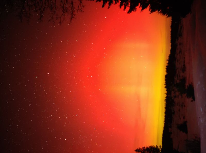 Auroras borealis sky night red yellow orange stars trees dark sunset horizon clouds mountains forest nature aurora atmosphere northern ight sky filled with vibrant colors. The sky is predominantly red, transitioning into a warm yellow hue near the horizon. The red color dominates the upper part of the image, while the yellow color is more prominent towards the bottom. The sky is dotted with numerous stars, adding a touch of sparkle to the scene. The horizon line is visible, separating the sky from the ground below. The ground is covered in snow, and there are silhouettes of trees and possibly a mountain range in the background. The overall atmosphere is serene and magical, with the colors creating a striking contrast against the dark sky.