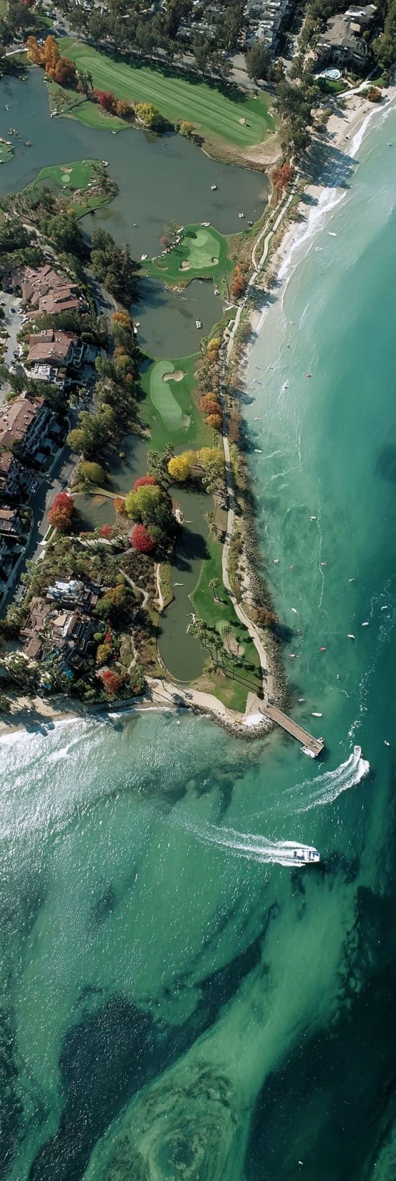 Aerien plage bateau batiment vert verdure maison terre ocean chemin gens plante complexe hotelier mer rivage ciel arbre golf parcours eau Une vue aérienne d'une zone côtière présentant un terrain de golf niché entre une plage de sable et un plan d'eau. Le terrain de golf est luxuriant et vert, avec des allées et des greens visibles. La plage est large et sablonneuse, avec un océan bleu clair en premier plan. Plusieurs bâtiments et maisons sont visibles en arrière-plan, dont certains sont entourés d'arbres et de buissons. Un bateau navigue sur l'eau, et il y a plusieurs petites îles au loin. Le ciel est clair et bleu, indiquant une journée ensoleillée.