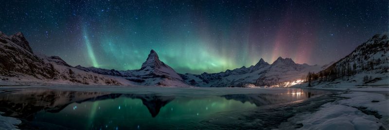 Mountains lake reflection night sky aurora stars snow winter nature ice rocks trees valley atmosphere weather a serene winter landscape is depicted under a vibrant night sky. Snow-covered mountains rise majestically in the background, their peaks dusted with snow. The sky is a canvas of deep blues and purples, dotted with countless stars. The aurora borealis, or northern lights, illuminates the sky with streaks of green, pink, and purple, creating a magical and ethereal atmosphere. The reflection of the aurora and stars dances on the surface of a calm, frozen lake in the foreground. The scene is tranquil and awe-inspiring, with the distant lights of a small town or village adding a touch of human presence to the wilderness.