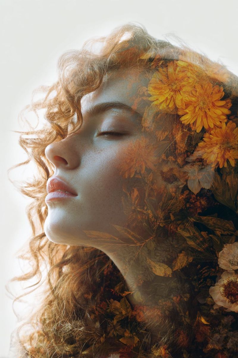 Femme fleurs beaute nature creatif inspiration esthetique Femme aux cheveux bouclés, brun-rouge, coiffés de manière à paraître entrelacés avec diverses fleurs et feuilles. Son visage est tourné de côté, et elle a les yeux fermés, donnant une expression sereine et paisible. Le fond derrière elle est un mélange de fleurs jaunes et orange vibrantes, ainsi que de feuilles vertes, créant un arrière-plan naturel et floral. La lumière semble venir de la gauche, projetant un doux éclat sur son visage et les fleurs, renforçant l'atmosphère onirique et éthérée de l'image.
