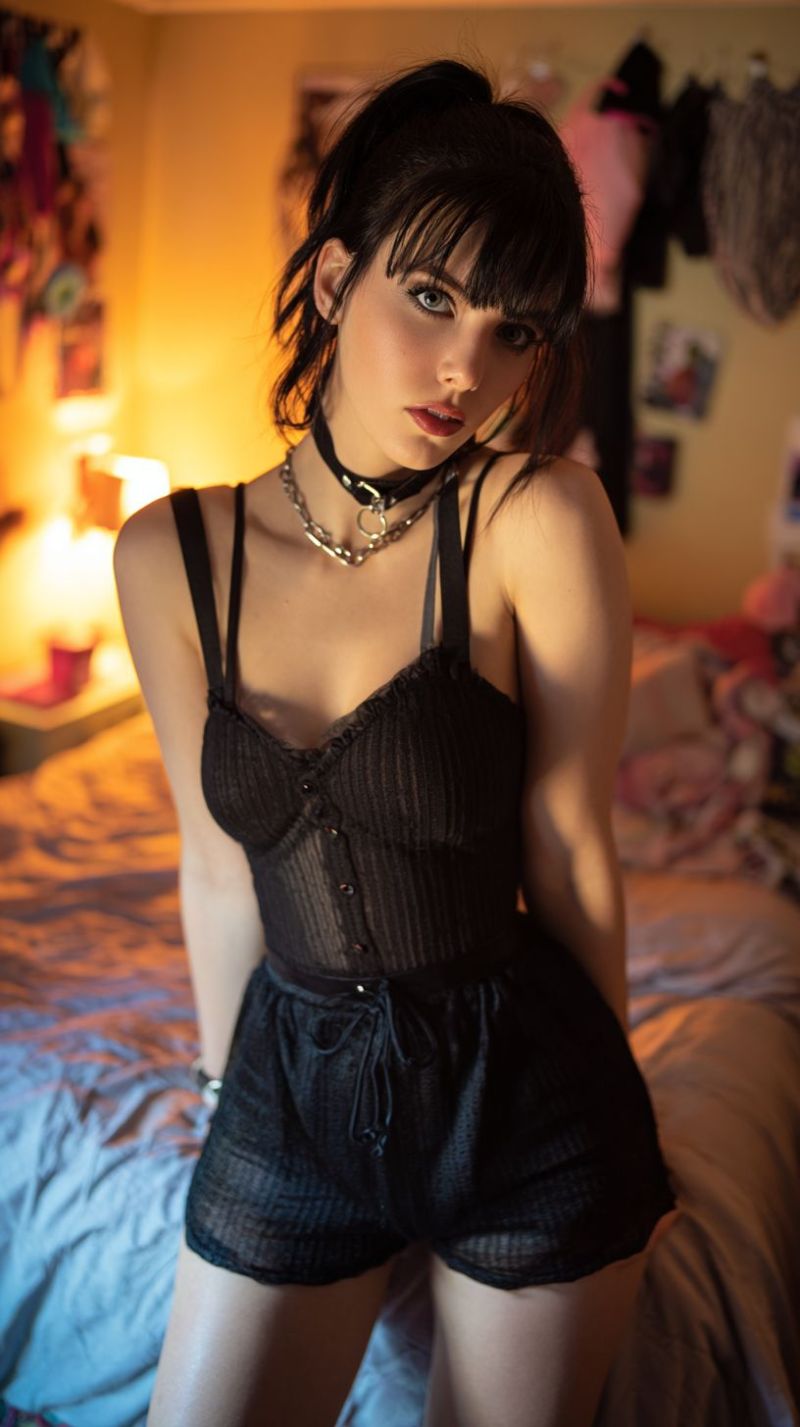 Femme piece lit nuit nuitee chambre dormir endormi zone temps endroit position posture disposition configuration environnement atmosphere ambiance Une femme aux cheveux courts noirs et aux franges est assise sur un lit, portant un corset en dentelle noire avec des boutons et un collier étouffant noir. Elle regarde sur le côté avec les lèvres légèrement ouvertes. La pièce a une lumière jaune chaude, et il y a des vêtements accrochés au mur. Sur le côté gauche, il y a une lampe et une petite table avec une tasse dessus.