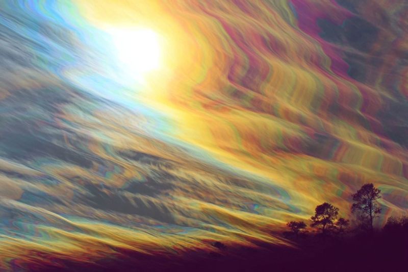 Ciel soleil nuages arc atmosphere nature arbres colline journee luminosite reflexion meteo environnement horizon L'image présente un ciel dramatique rempli de nuages tourbillonnants et vibrants qui affichent un spectre de couleurs incluant jaune, orange, rose et bleu. Le soleil est situé au centre, brillant intensément et projetant une lumière chaude et dorée qui illumine les nuages, créant un effet radieux. Les nuages sont épais et texturés, avec certaines zones apparaissant plus solides et d'autres plus translucides. Sous les nuages, il y a des silhouettes d'arbres, qui sont sombres et semblent être sur une colline ou une zone surélevée. La scène globale est dynamique et colorée, avec un sentiment de mouvement et d'énergie dans le ciel.