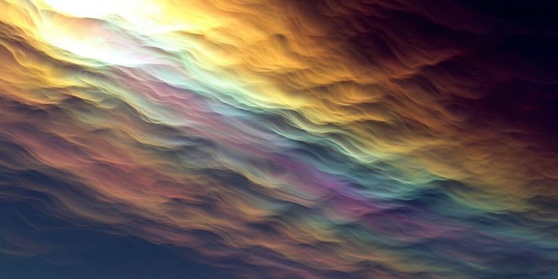 Ciel nuages atmosphere meteo nature texture design degrade saturation luminosite L'image présente un ciel abstrait vibrant, rempli de nuages tourbillonnants et ondulants. Les nuages sont un mélange de couleurs chaudes et froides, incluant des nuances de jaune, orange, rose, violet et bleu. Les couleurs se mélangent harmonieusement, créant une apparence dynamique et fluide. Le ciel semble en mouvement, avec des nuages formant des vagues et des ondulations qui suggèrent une sensation de profondeur et de texture. L'effet global est celui d'un paysage surréaliste et onirique, avec une sensation de mouvement et d'énergie.