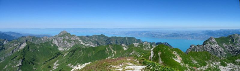 Montagne ciel lac eau colline vallee crete pic chaine sommet glaciers glaciologie D'un point de vue élevé, une vue panoramique d'un paysage montagneux se déploie. L'avant-plan présente un terrain rocailleux et accidenté avec des taches de végétation verte vibrante. Les montagnes s'élèvent abruptement, leurs pentes parsemées de plantes et d'arbustes robustes. Au loin, un grand plan d'eau, probablement un lac, brille sous le ciel bleu clair. Le ciel lui-même est d'un bleu profond et sans nuages, indiquant une journée ensoleillée. L'horizon est parsemé de montagnes plus lointaines, créant un sentiment de profondeur et d'échelle. La scène globale est sereine et majestueuse, mettant en valeur la beauté de la nature depuis une haute altitude.