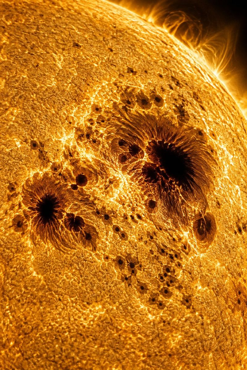 Sun solar astronomy space cosmos star universe astrophysics telescope observation science celestial sunspots activity flares surface prominence wind The image shows the surface of the Sun, which is predominantly golden-yellow with a textured, mottled appearance. There are numerous dark spots scattered across the surface, varying in size and shape. Some of these spots are circular and well-defined, while others are irregular and blend into the surrounding texture. The surface has a dynamic, almost turbulent look, with swirling patterns and hints of movement. The overall effect is one of intense heat and energy, with the Sun's surface appearing both rough and smooth in different areas.