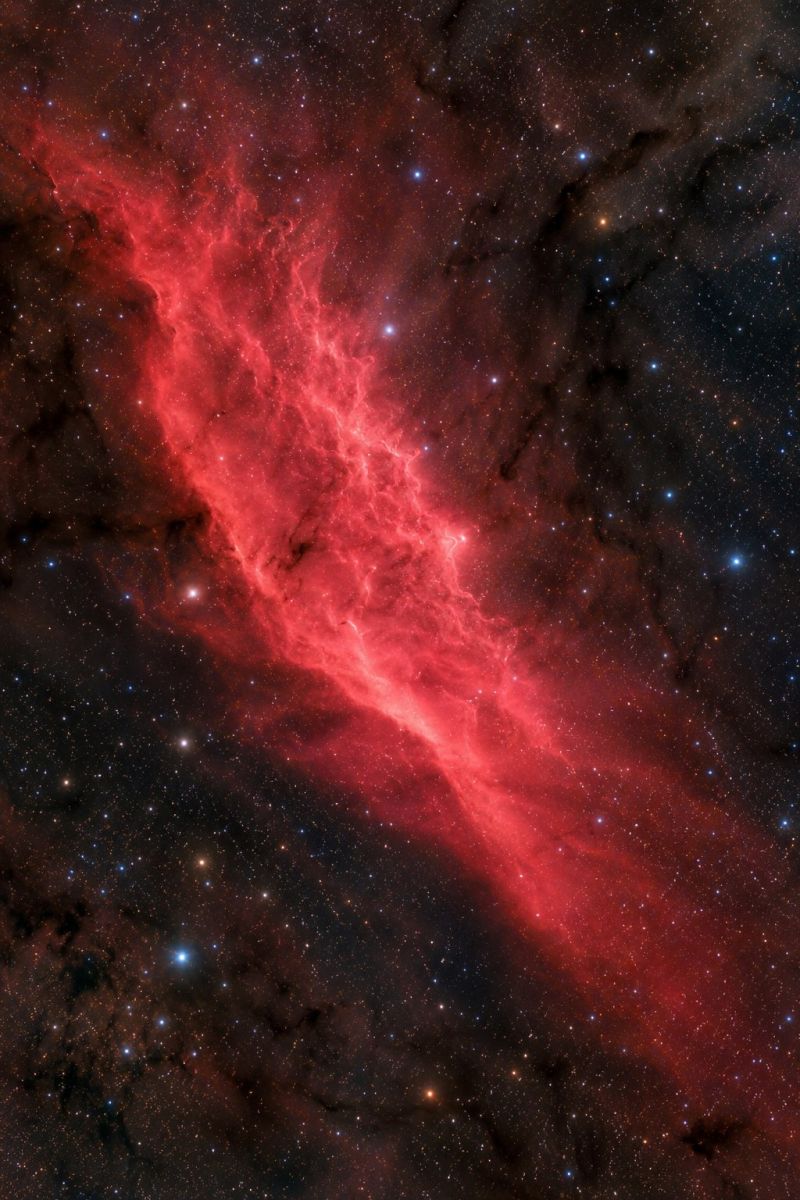 Nebula astronomy space universe galaxy star cosmic celestial cosmology astrophysics astrophotography night sky outer starry cluster dust formation The image showcases a striking nebula in deep space, primarily colored in vibrant reds and oranges. The nebula appears as a long, flowing structure with intricate, wispy patterns that resemble a cosmic river or a fiery dragon. It is set against a dark, almost black background, which makes the nebula's colors stand out more vividly. Scattered throughout the image are numerous small, bright stars, some of which are blue, adding contrast to the red hues of the nebula. The overall scene is both ethereal and majestic, evoking a sense of the vastness and mystery of the universe.