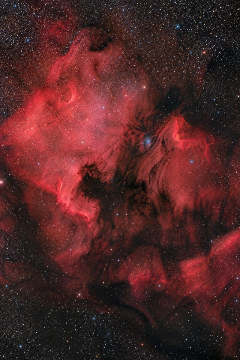 Nebuleuse astronomie espace univers etoile galaxie cosmique celeste astrophotographie nuit ciel obscurite poussiere amas rouge nuage formation interst L'image montre une nébuleuse, principalement dans des tons rouge foncé, avec des motifs ondulés complexes ressemblant à un nuage ou à de la fumée. La nébuleuse est entourée d'un fond sombre, presque noir, créant un contraste saisissant. De nombreuses petites étoiles brillantes, dont l'intensité varie, sont éparpillées sur l'image et ajoutent un effet scintillant à la scène. La nébuleuse elle-même possède une structure complexe, certaines zones semblant plus denses et d'autres plus translucides, ce qui lui confère un aspect dynamique et texturé.