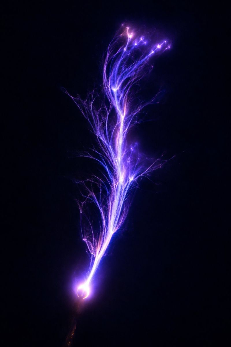 Foudre electricite etincelle plasma decharge energie puissance tension courant science experience technologie innovation experimentation recherche dec Une image saisissante d'un éclair violet sur un fond sombre. L'éclair se divise en plusieurs petits éclairs, créant ainsi une structure arborescente. Les branches sont fines et complexes, avec une qualité rougeoyante, presque éthérée. La partie centrale de l'éclair est brillante et intense, tandis que les branches s'estompent dans l'obscurité. L'effet global est fascinant et surnaturel.
